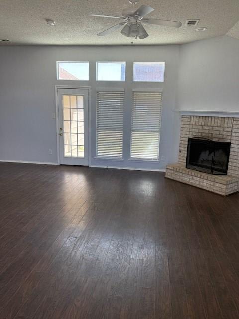 unfurnished living room featuring a ceiling fan, a brick fireplace, visible vents, and dark wood-style flooring