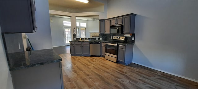 kitchen with gray cabinets, decorative backsplash, appliances with stainless steel finishes, wood finished floors, and baseboards