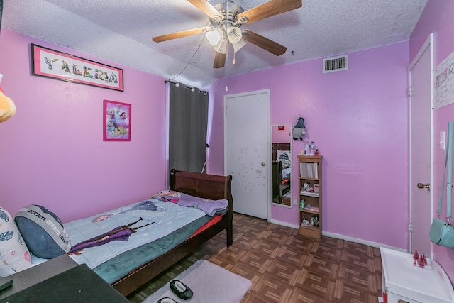 bedroom with a textured ceiling, dark parquet flooring, and ceiling fan