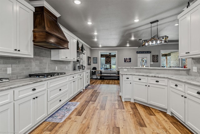 kitchen with stainless steel gas stovetop, custom exhaust hood, and white cabinetry