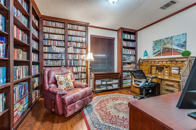 office space featuring wall of books, wood finished floors, visible vents, and crown molding