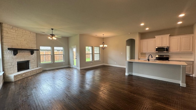 kitchen featuring appliances with stainless steel finishes, a fireplace, hanging light fixtures, a kitchen island with sink, and white cabinets