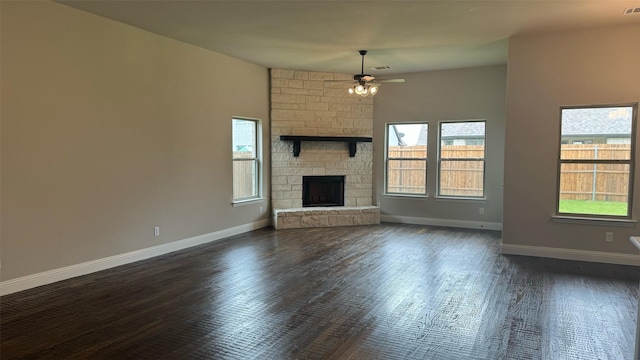 unfurnished living room featuring ceiling fan, a stone fireplace, and dark hardwood / wood-style flooring