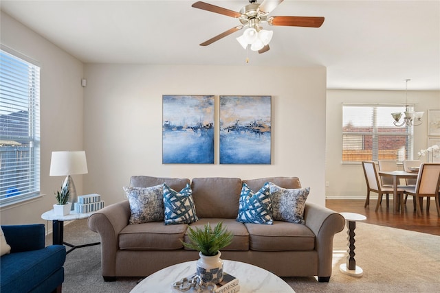 living room with ceiling fan with notable chandelier, carpet floors, and baseboards