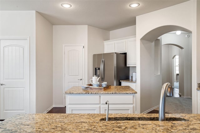 kitchen featuring stainless steel fridge, sink, white cabinetry, light stone countertops, and a kitchen island