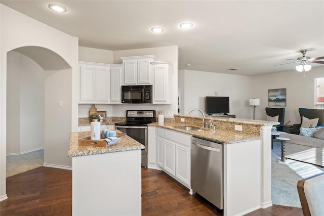 kitchen with appliances with stainless steel finishes, open floor plan, white cabinets, a sink, and light stone countertops