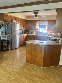 kitchen featuring ceiling fan, stainless steel refrigerator, kitchen peninsula, and light hardwood / wood-style floors