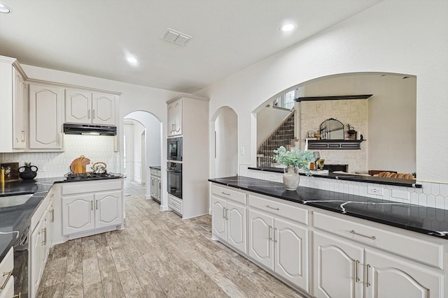 kitchen with dark countertops, white cabinets, built in microwave, oven, and under cabinet range hood