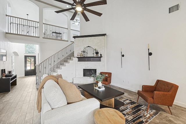 living room featuring a stone fireplace, wood finished floors, a towering ceiling, visible vents, and stairs