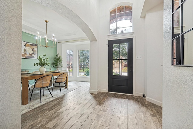 entryway featuring an inviting chandelier, wood tiled floor, baseboards, and arched walkways