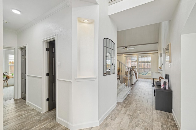 hall featuring light wood-style floors, baseboards, stairs, and ornamental molding