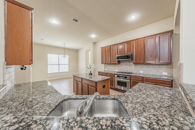 kitchen featuring stainless steel appliances, dark stone counters, decorative backsplash, sink, and hanging light fixtures