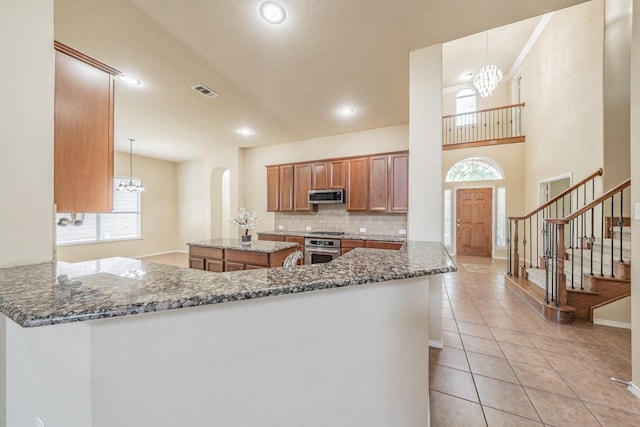 kitchen with a notable chandelier, stainless steel appliances, kitchen peninsula, and decorative light fixtures