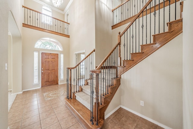 tiled foyer entrance featuring crown molding, a towering ceiling, and a notable chandelier