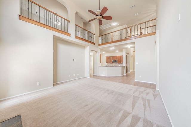 unfurnished living room featuring ceiling fan, light carpet, and a towering ceiling