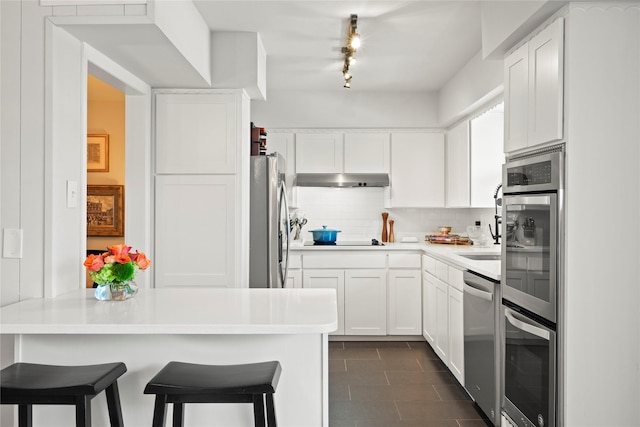 kitchen featuring dark tile patterned flooring, white cabinets, appliances with stainless steel finishes, backsplash, and a breakfast bar area