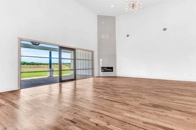 unfurnished living room featuring light hardwood / wood-style floors, a chandelier, and a towering ceiling