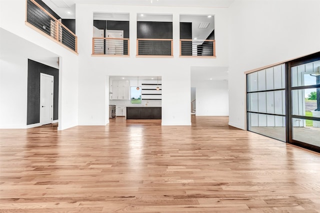 unfurnished living room with light hardwood / wood-style floors and a towering ceiling