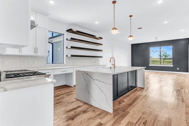 kitchen featuring decorative light fixtures, white cabinetry, light stone countertops, and an island with sink