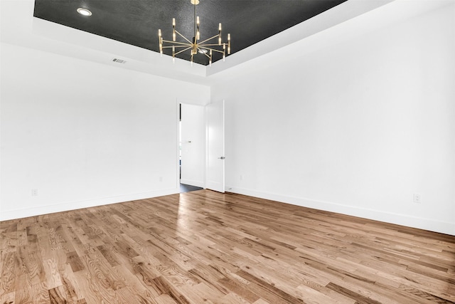 empty room featuring a raised ceiling, an inviting chandelier, and light hardwood / wood-style floors