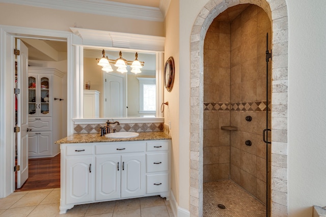 bathroom with crown molding, vanity, a shower with door, tile patterned flooring, and backsplash