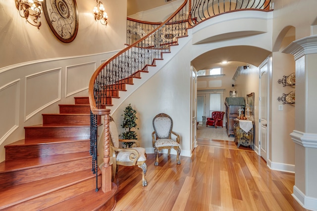 staircase with decorative columns, a towering ceiling, and wood-type flooring