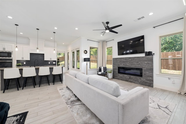 living room with sink, a stone fireplace, light hardwood / wood-style flooring, and plenty of natural light