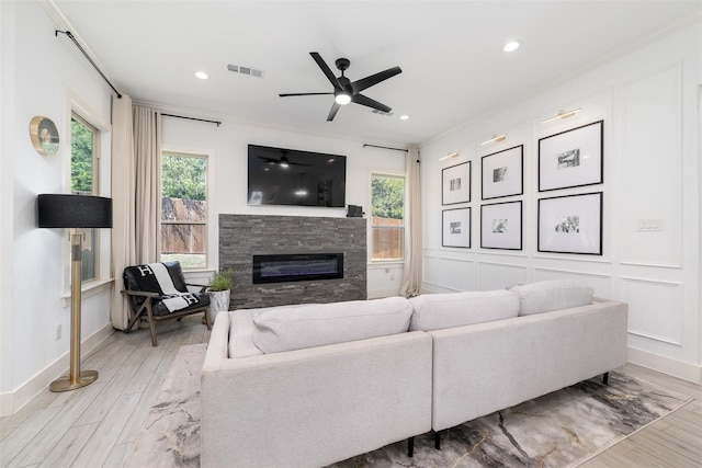 living room with a stone fireplace, light hardwood / wood-style flooring, plenty of natural light, and crown molding