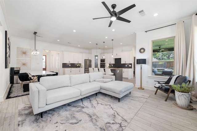 living room with ceiling fan with notable chandelier, ornamental molding, and light hardwood / wood-style floors