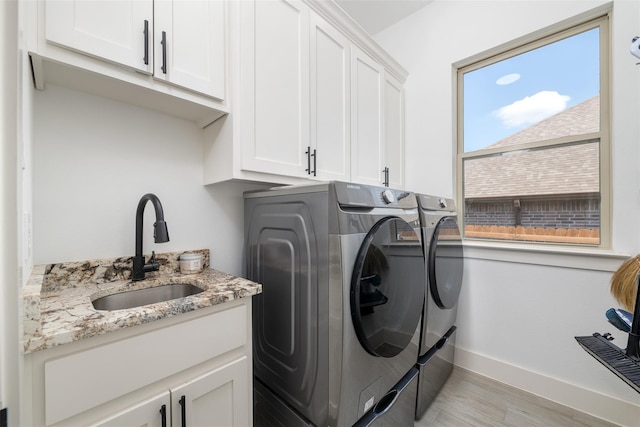 clothes washing area featuring cabinets, sink, washing machine and dryer, and light hardwood / wood-style floors