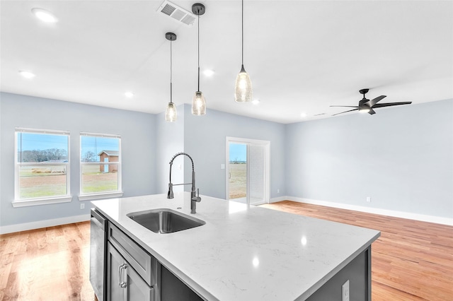 kitchen with open floor plan, decorative light fixtures, stainless steel dishwasher, light wood-style floors, and a sink