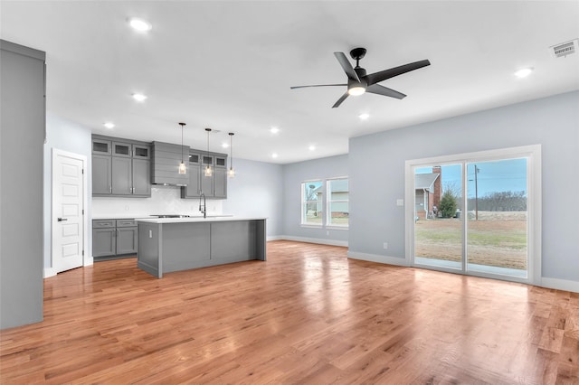 kitchen with light wood finished floors, tasteful backsplash, visible vents, an island with sink, and gray cabinets