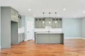 kitchen with light hardwood / wood-style floors, pendant lighting, gray cabinets, and a kitchen island with sink