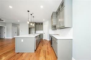 kitchen with dishwasher, light hardwood / wood-style flooring, pendant lighting, a center island with sink, and gray cabinets