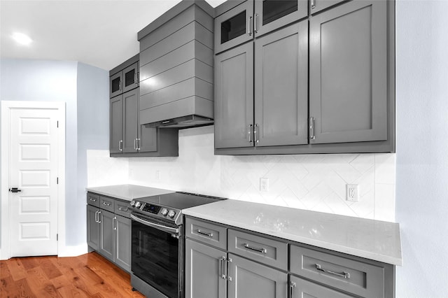 kitchen featuring stainless steel electric range oven, glass insert cabinets, gray cabinets, light wood-style floors, and backsplash