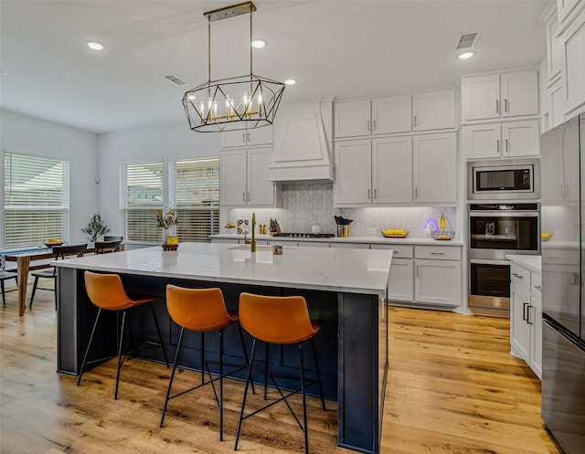 kitchen featuring decorative light fixtures, white cabinets, a kitchen island with sink, and custom exhaust hood