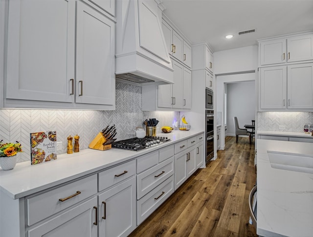 kitchen with decorative backsplash, white cabinetry, stainless steel appliances, and custom range hood