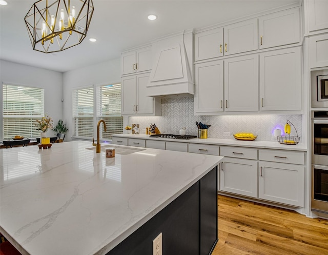 kitchen featuring custom range hood, hanging light fixtures, white cabinetry, sink, and light hardwood / wood-style flooring