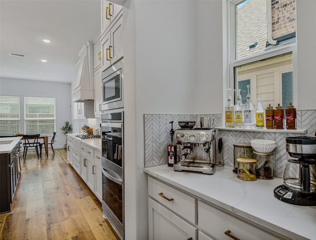 kitchen with white cabinets, appliances with stainless steel finishes, tasteful backsplash, light hardwood / wood-style floors, and light stone counters