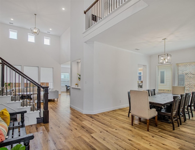 dining space with crown molding, light wood-type flooring, a high ceiling, and an inviting chandelier