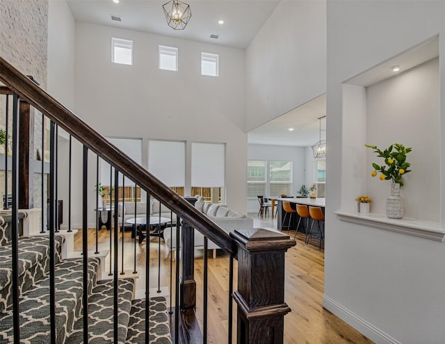 stairs featuring hardwood / wood-style floors, a towering ceiling, and a notable chandelier