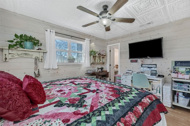 bedroom with ceiling fan, wood finished floors, an ornate ceiling, and wooden walls