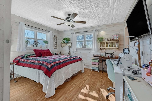 bedroom featuring wooden walls, multiple windows, an ornate ceiling, and light wood-style floors