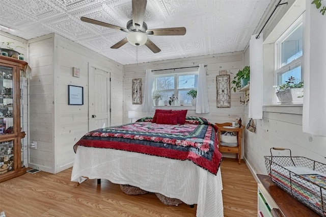 bedroom with an ornate ceiling, light wood-type flooring, wooden walls, and a ceiling fan