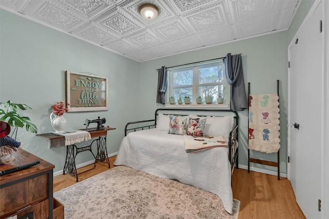 bedroom with wood finished floors, an ornate ceiling, and baseboards