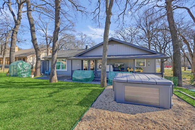 rear view of house with a hot tub and a lawn