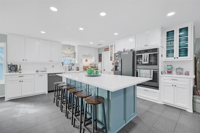 kitchen featuring white cabinets, a kitchen island, a kitchen breakfast bar, stainless steel appliances, and light countertops