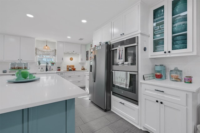 kitchen with light countertops, appliances with stainless steel finishes, glass insert cabinets, white cabinets, and a sink