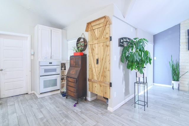 kitchen with white double oven, white cabinetry, light wood-type flooring, and vaulted ceiling