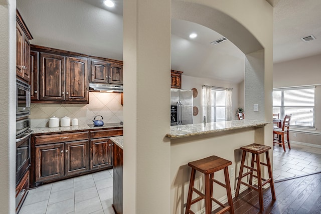 kitchen featuring a kitchen breakfast bar, tasteful backsplash, light stone countertops, and appliances with stainless steel finishes